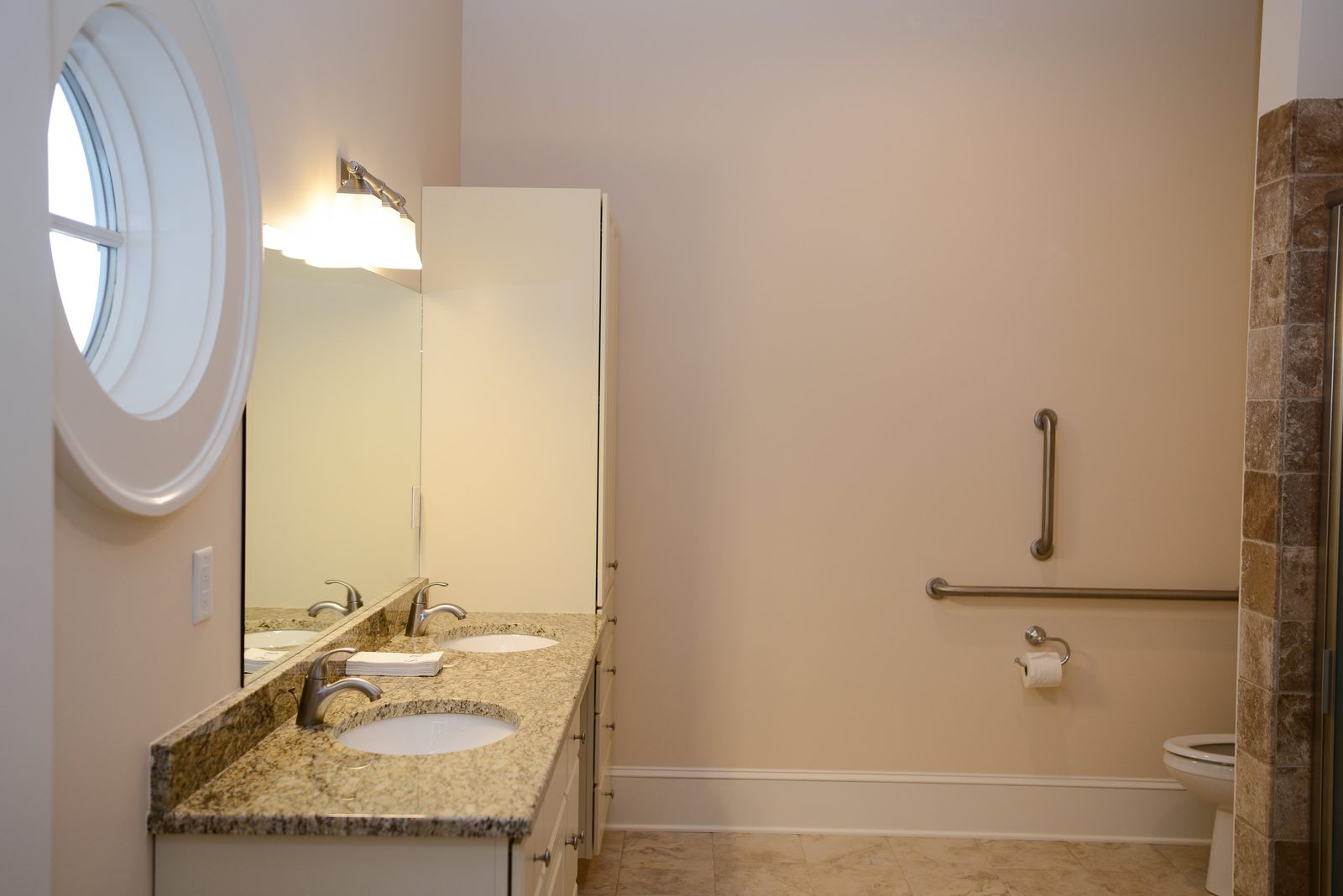 An accessible bathroom with grab bars, a wide vanity and a round window