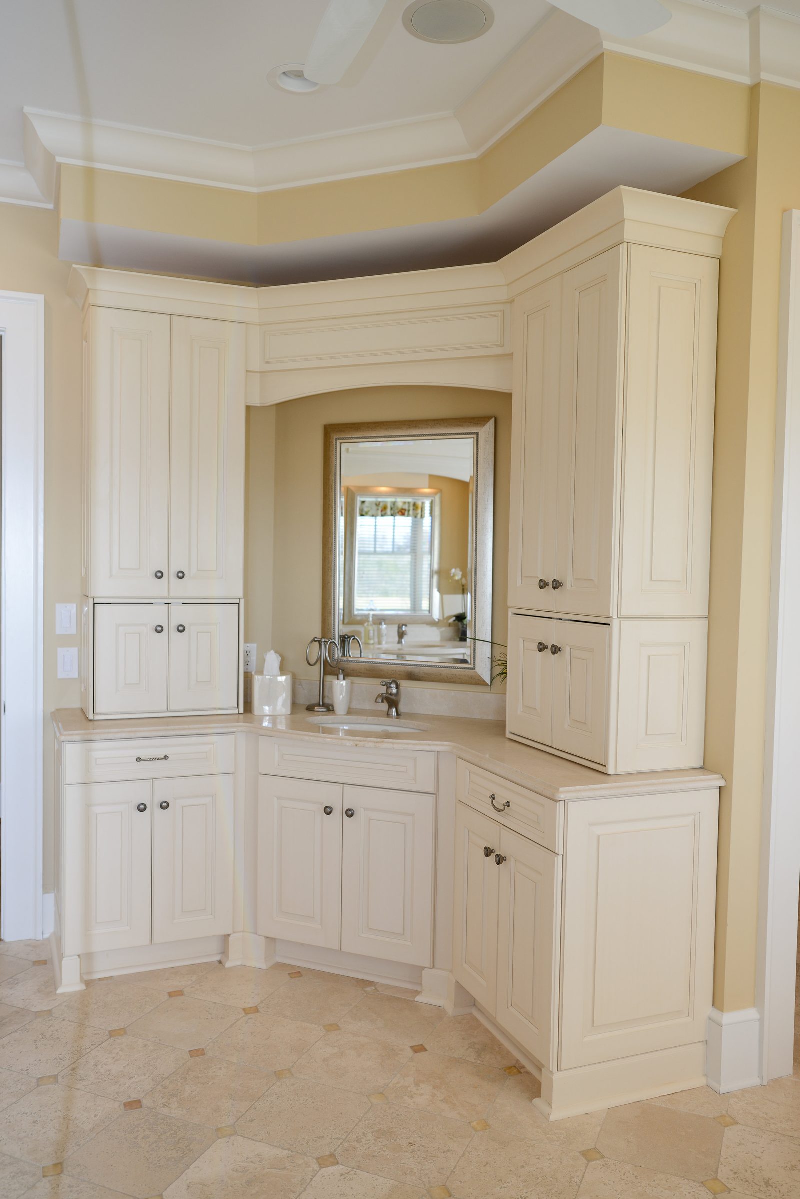 A bathroom corner vanity with a mirror and white cabinetry