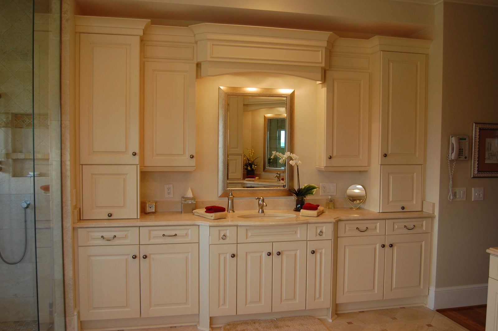 A bathroom with cream cabinetry, a vanity mirror and a glass shower