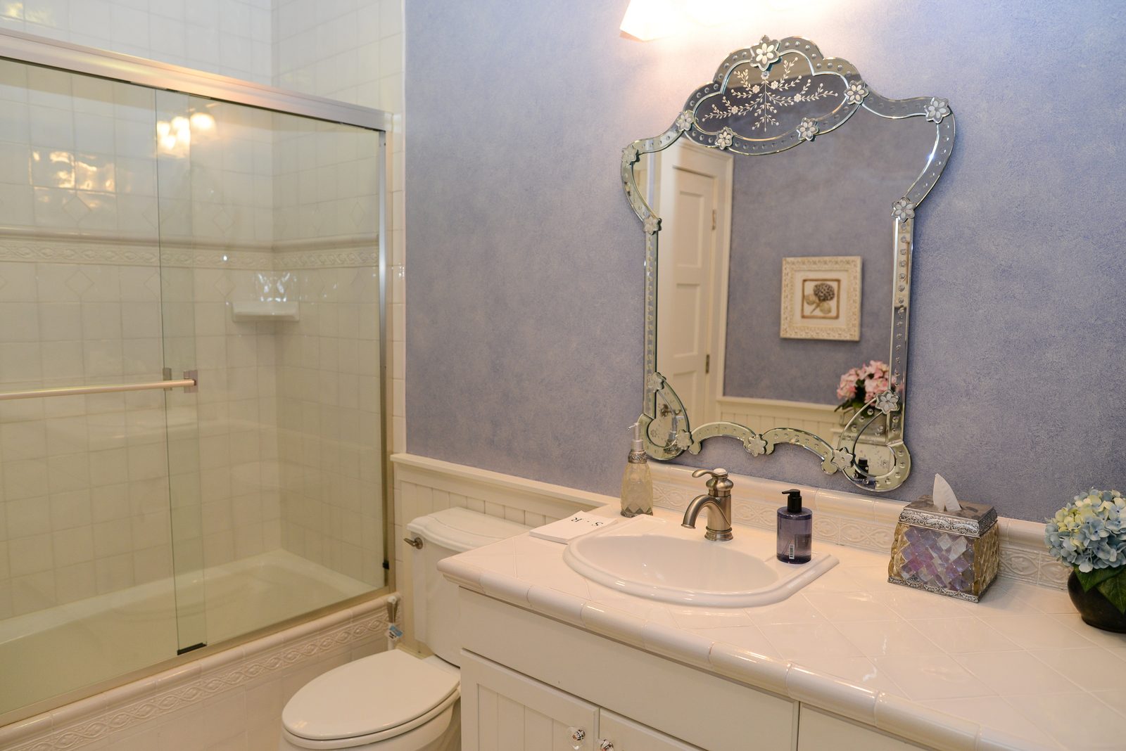 A guest bathroom with lavender walls, a glass shower and an ornate mirror (view 1)