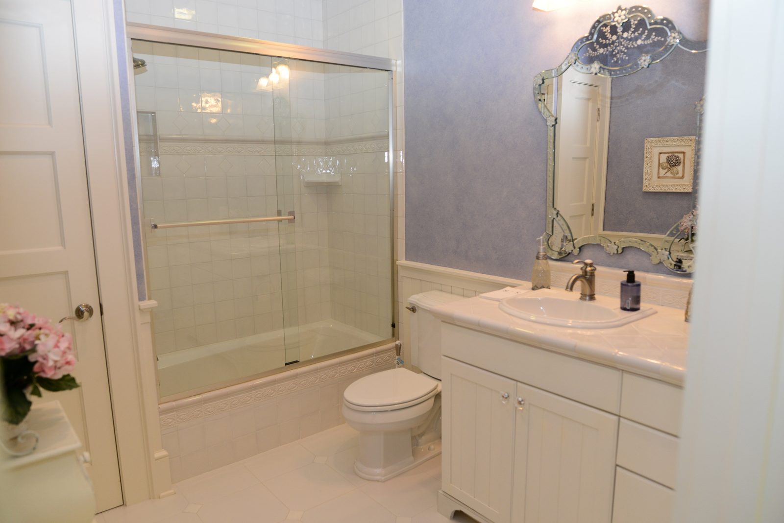 A guest bathroom with lavender walls, a glass shower and an ornate mirror (view 2)
