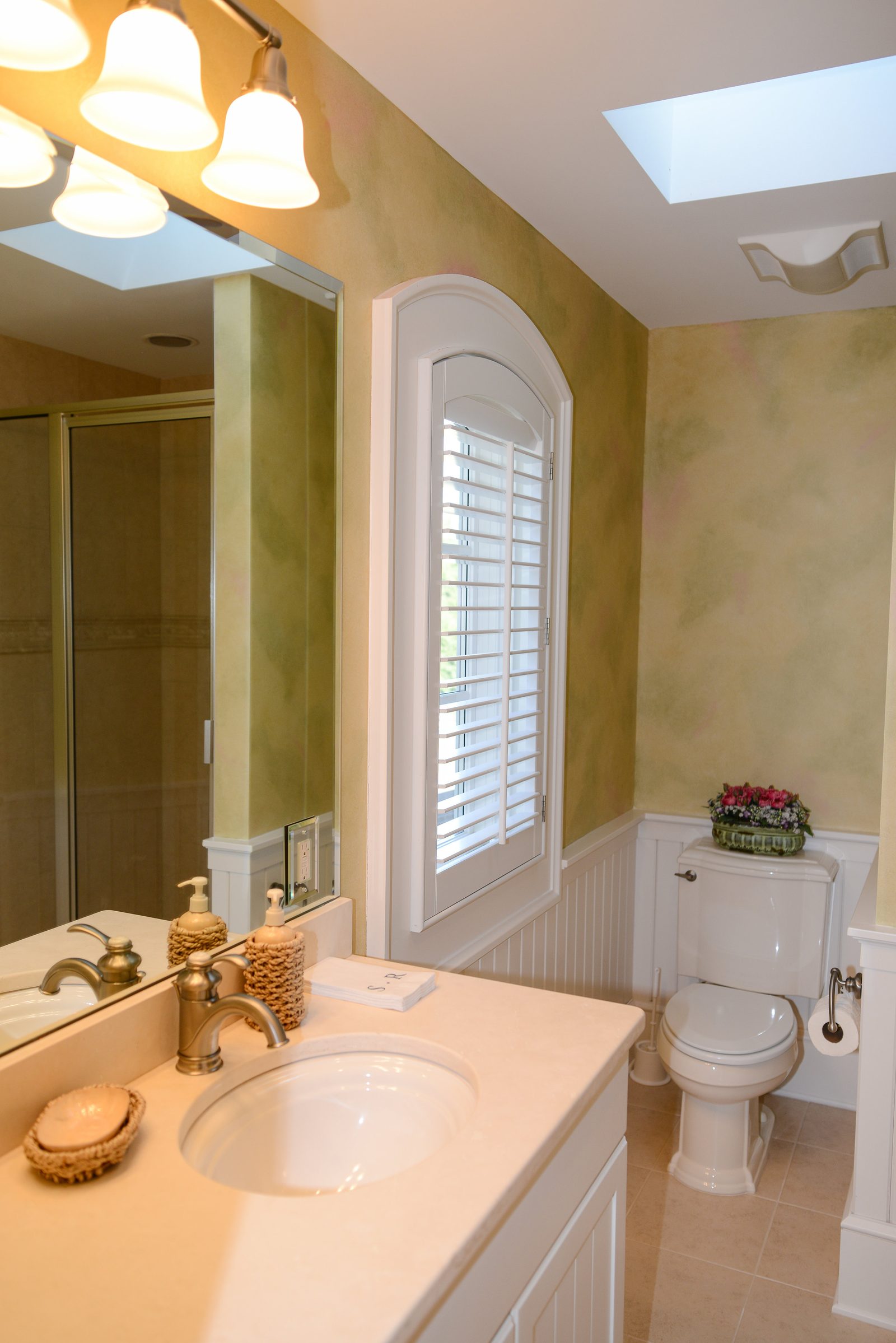 A guest bathroom lit by a skylight, with a vanity and arched window (view 1)