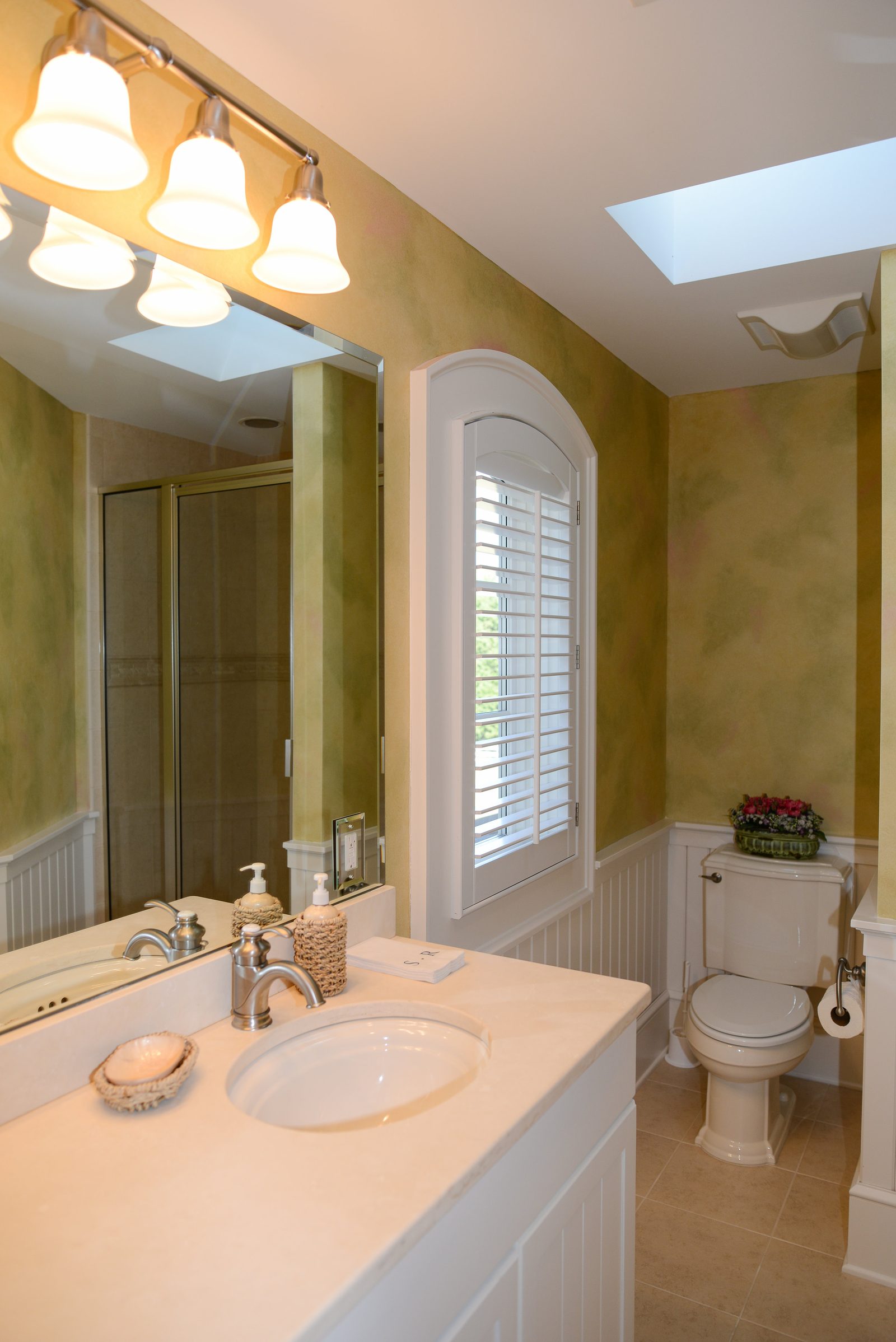 A guest bathroom lit by a skylight, with a vanity and arched window (view 2)