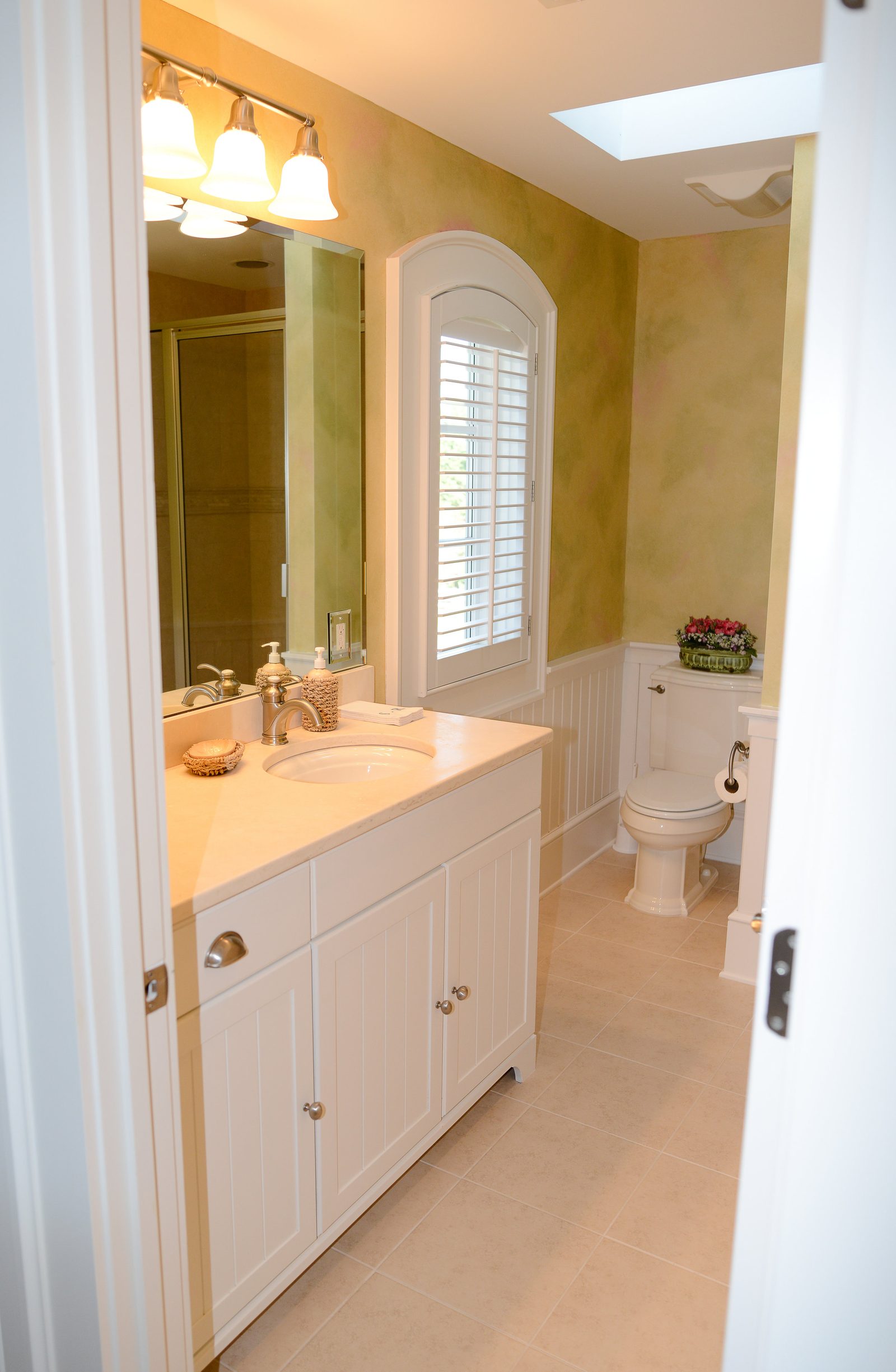 A guest bathroom lit by a skylight, with a vanity and arched window (view 3)
