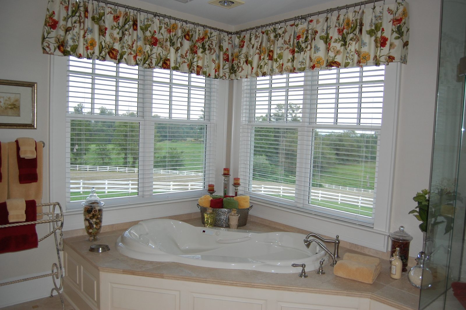 A bathroom with a corner tub set beneath a bank of shuttered windows