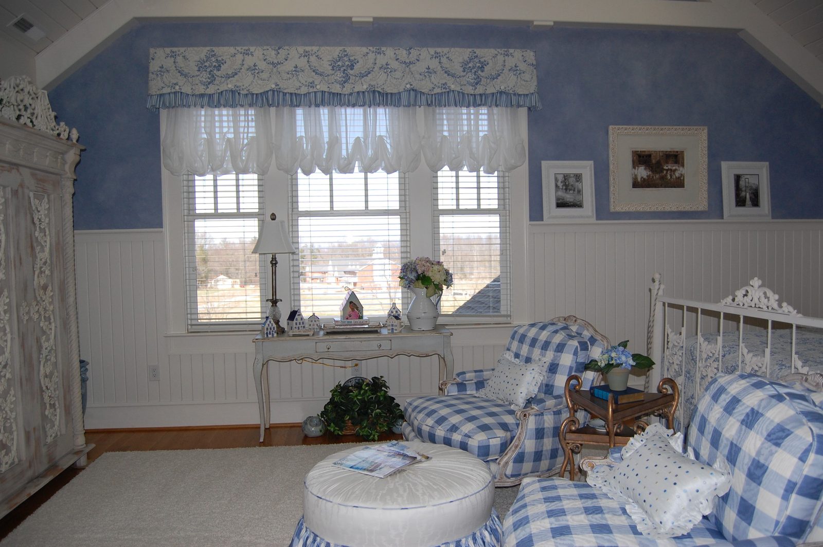 A bedroom with blue checked seating, an iron bed and a painted chest (view 1)