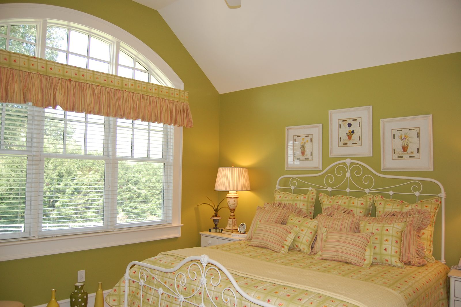 A bedroom with a white iron bed, green walls and windows overlooking the trees