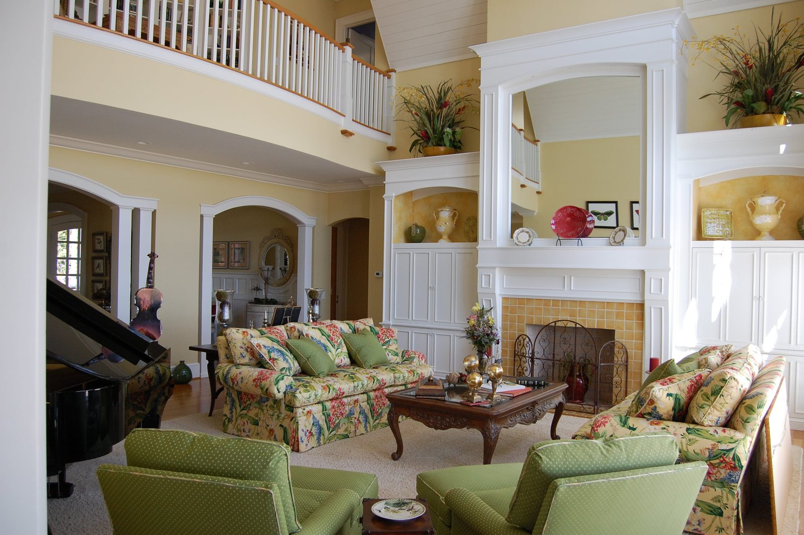 A commons room with a fireplace, floral sofas and a grand piano beyond