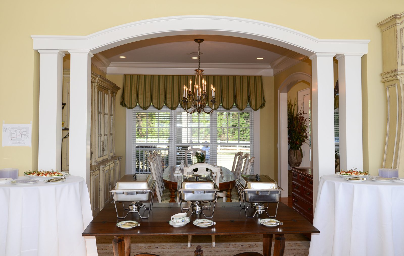 The dining room seen through a columned archway, with a chandelier over a long table