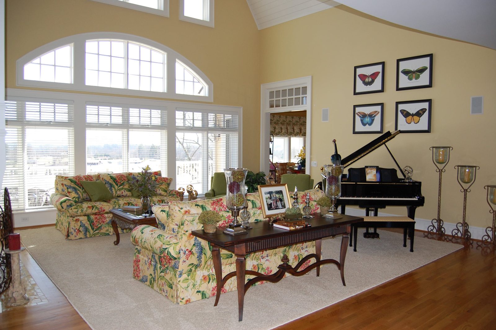 The great room with floral sofas, a grand piano and a wall of arched windows