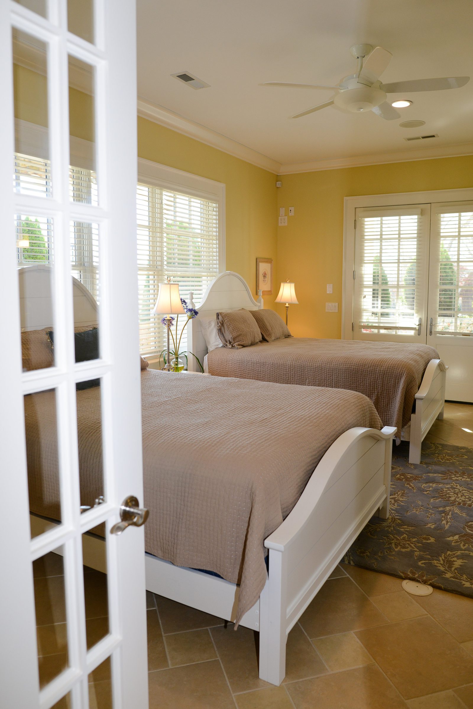 A guest room seen through open French doors, with a white bed and tile entry