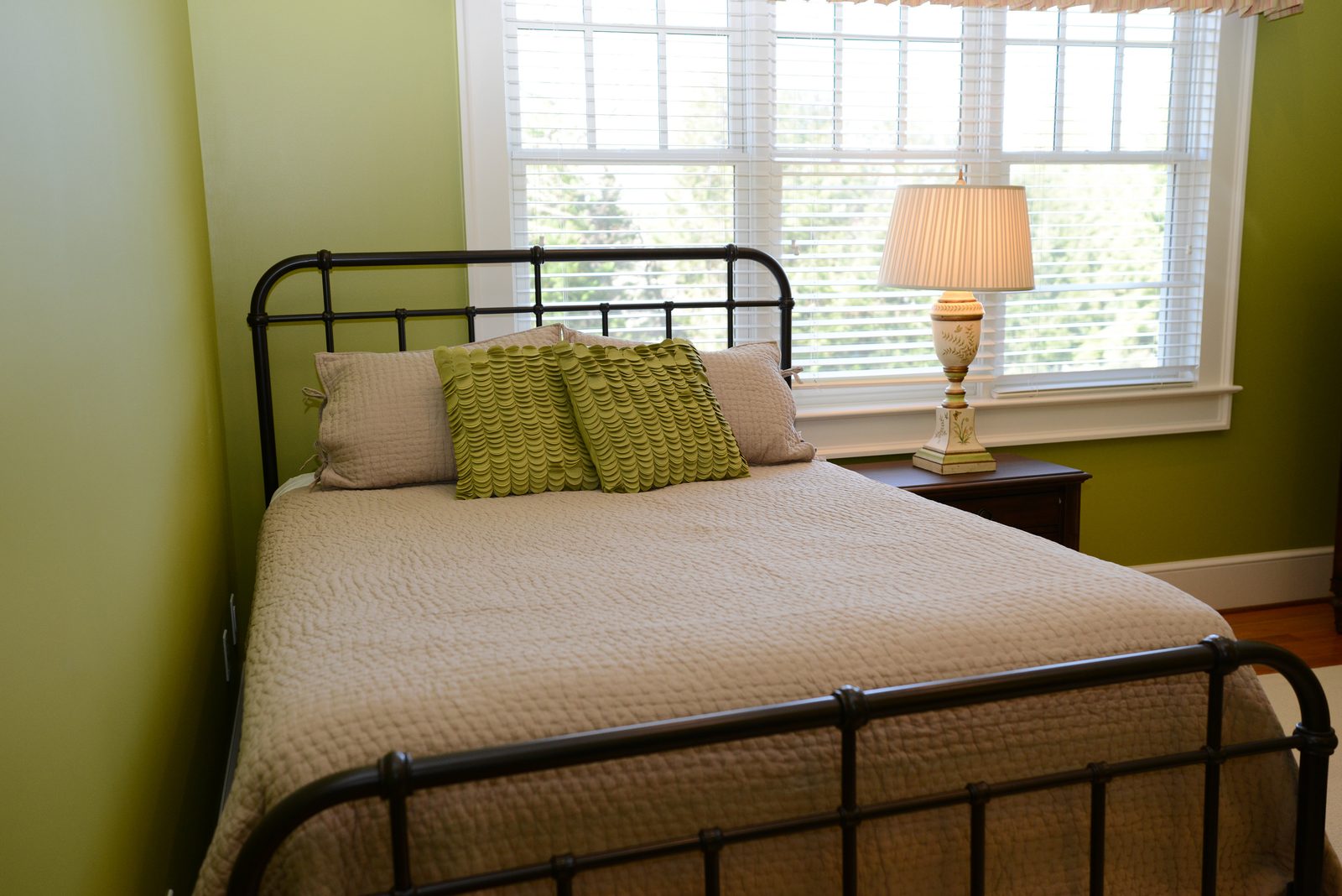 A guest room with an iron bed, green walls and a valanced window (view 2)