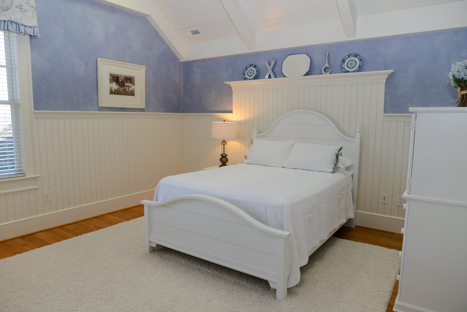 A guest room with a white bed, beadboard wainscot and lavender walls (view 1)