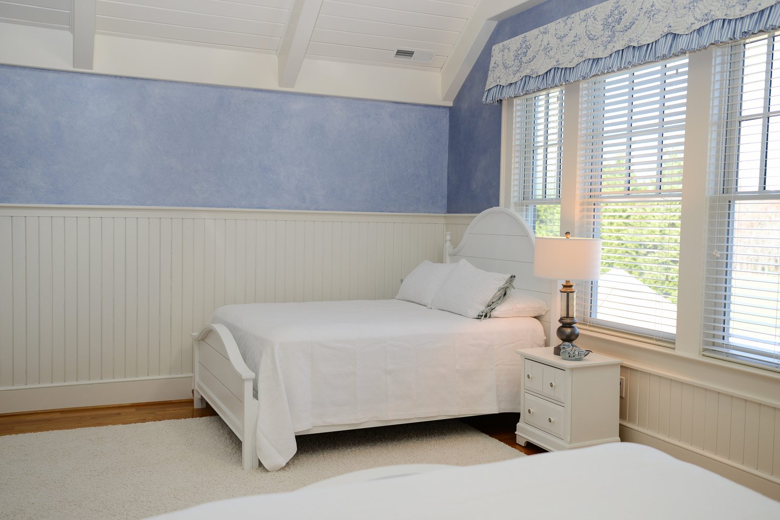 A guest room with a white bed, beadboard wainscot and lavender walls (view 2)