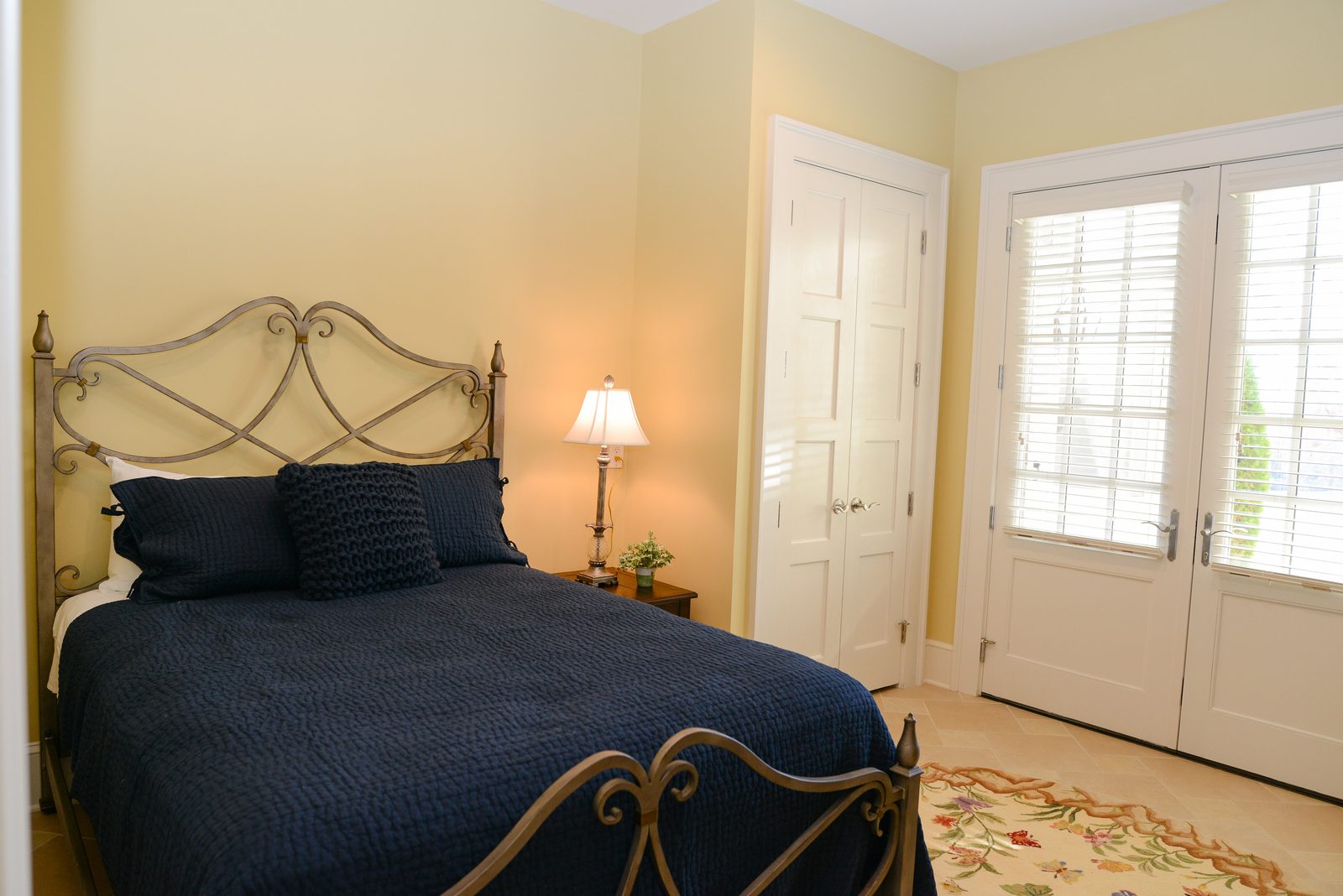 A guest room with an iron bed dressed in navy linens, a lamp and a nightstand (view 2)