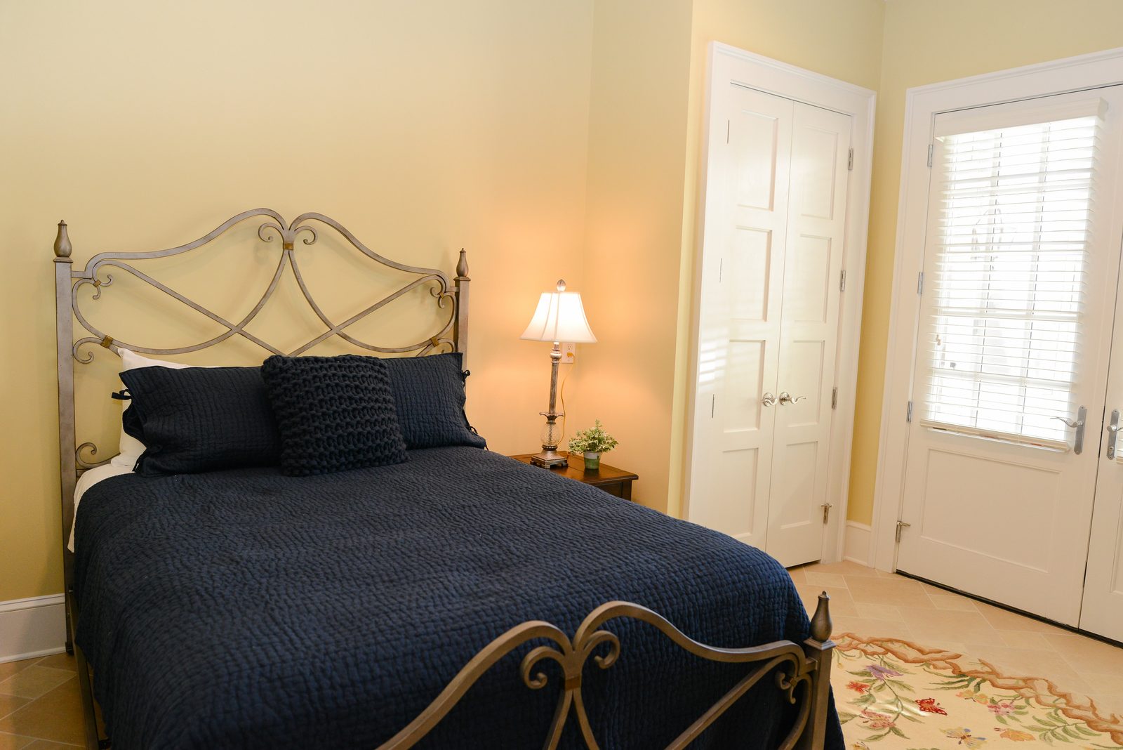 A guest room with an iron bed dressed in navy linens, a lamp and a nightstand (view 3)
