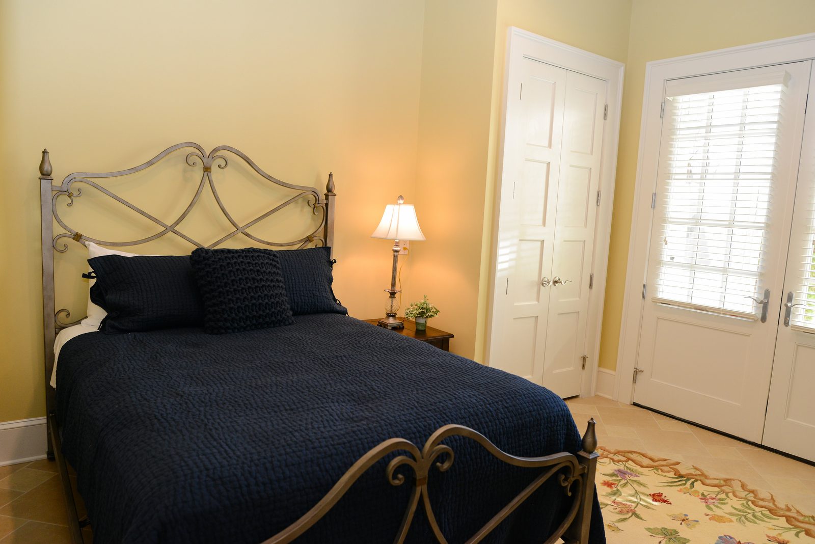 A guest room with an iron bed dressed in navy linens, a lamp and a nightstand (view 4)