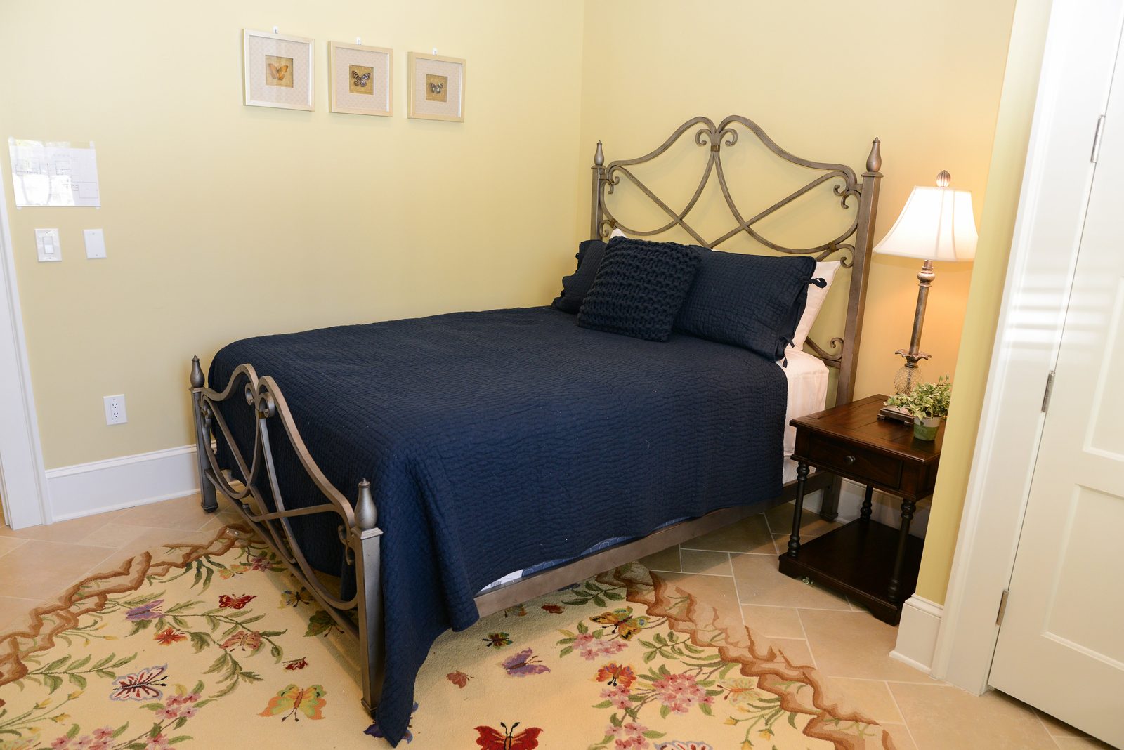 A guest room with an iron bed dressed in navy linens, a lamp and a nightstand (view 5)