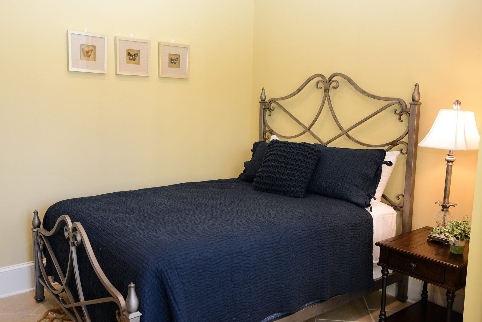 A guest room with an iron bed dressed in navy linens, a lamp and a nightstand (view 6)