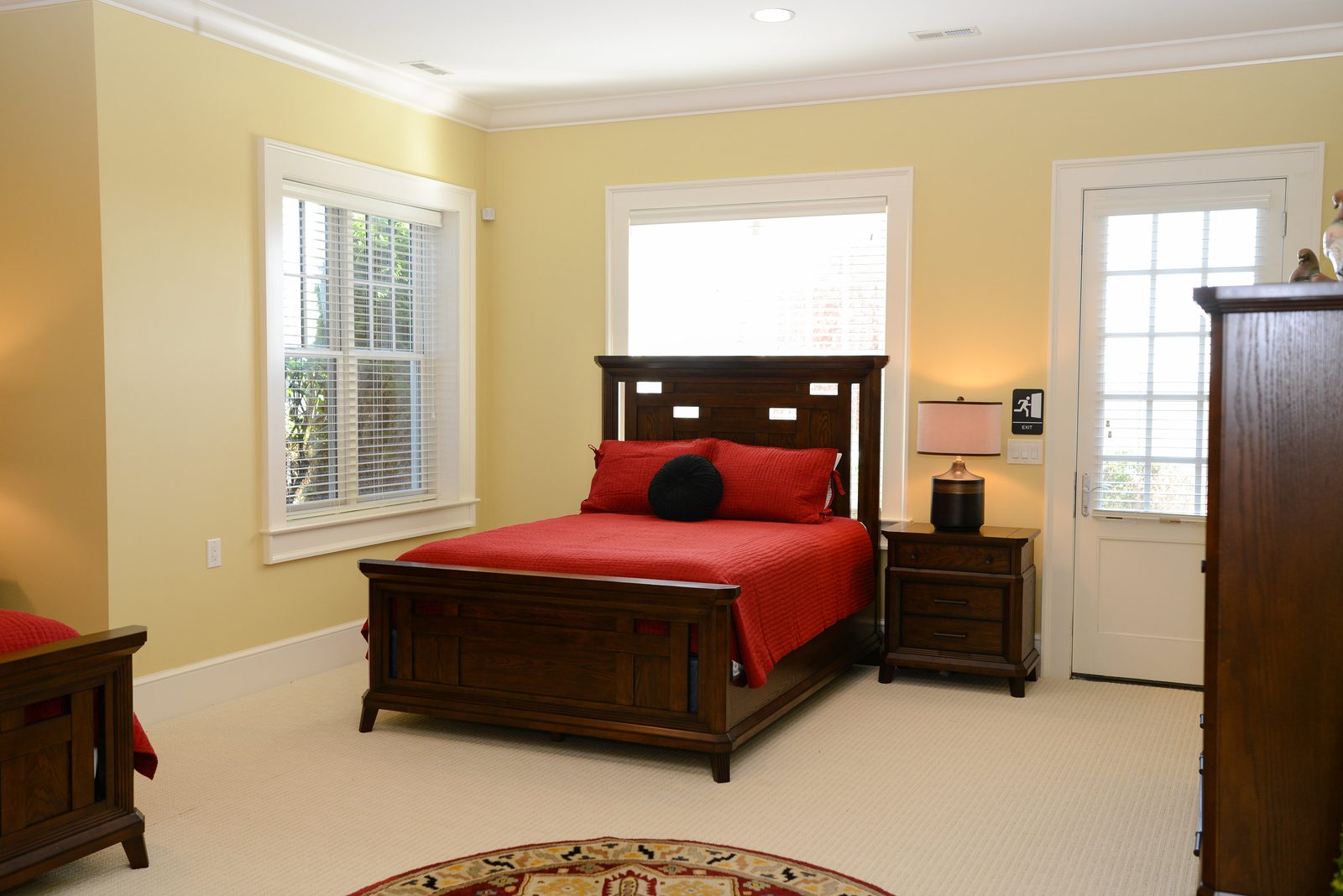 A guest room with red-linened beds, a dresser and a door to the grounds (view 1)