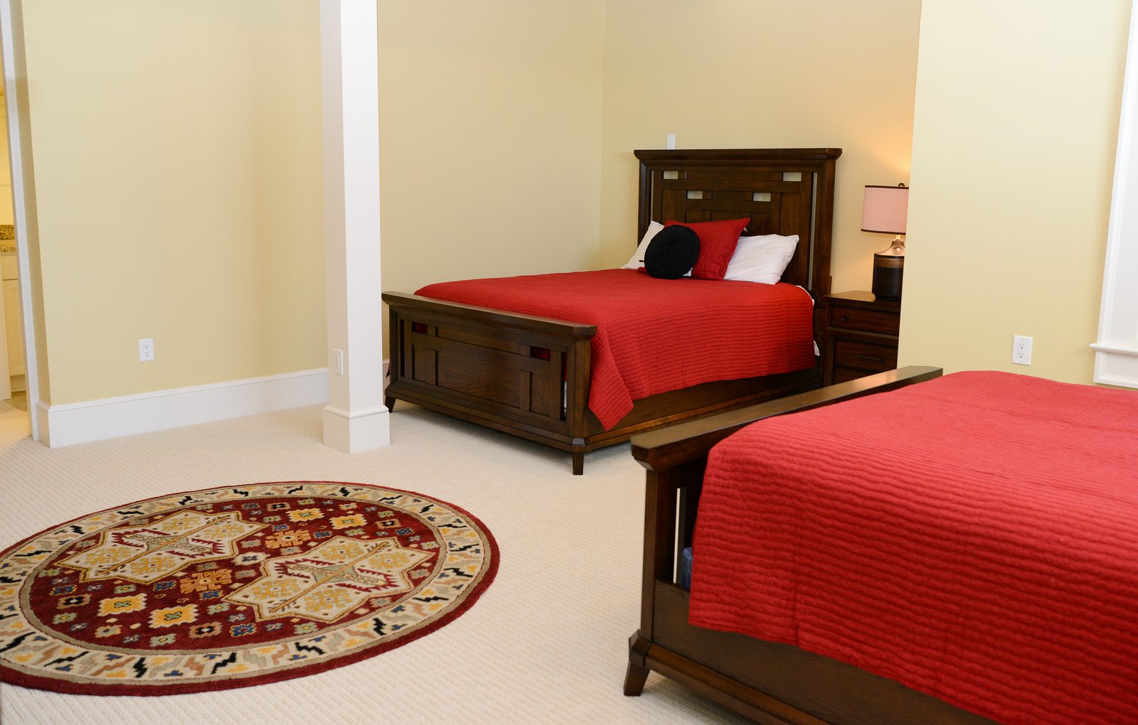 A guest room with red-linened beds, a dresser and a door to the grounds (view 2)