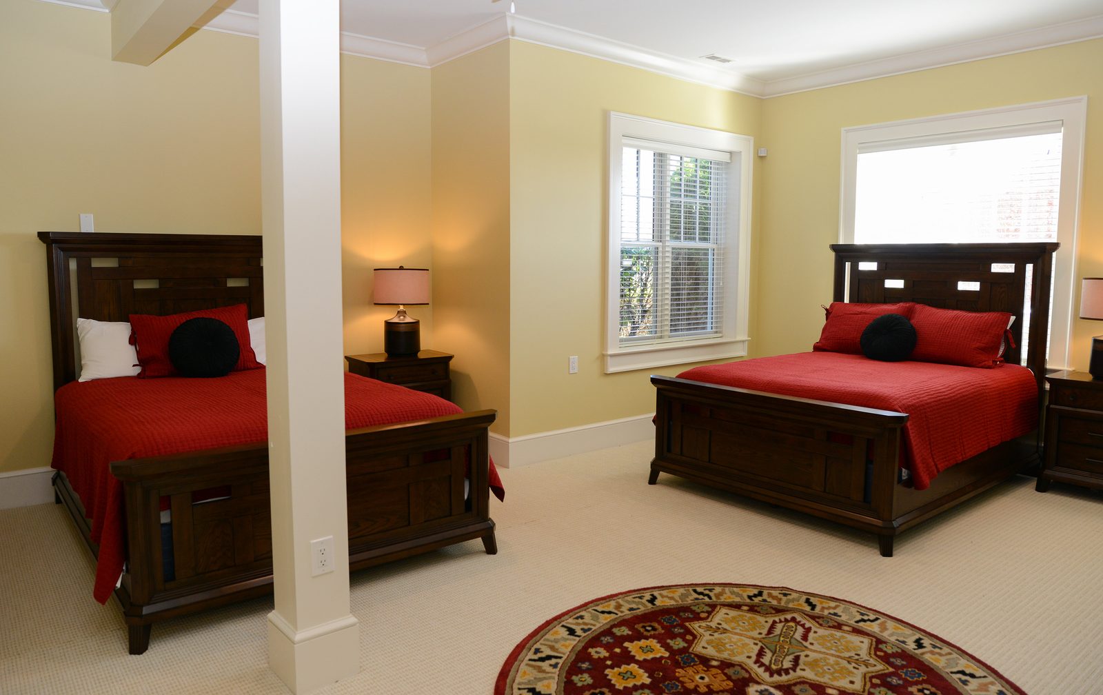 A guest room with red-linened beds, a dresser and a door to the grounds (view 3)