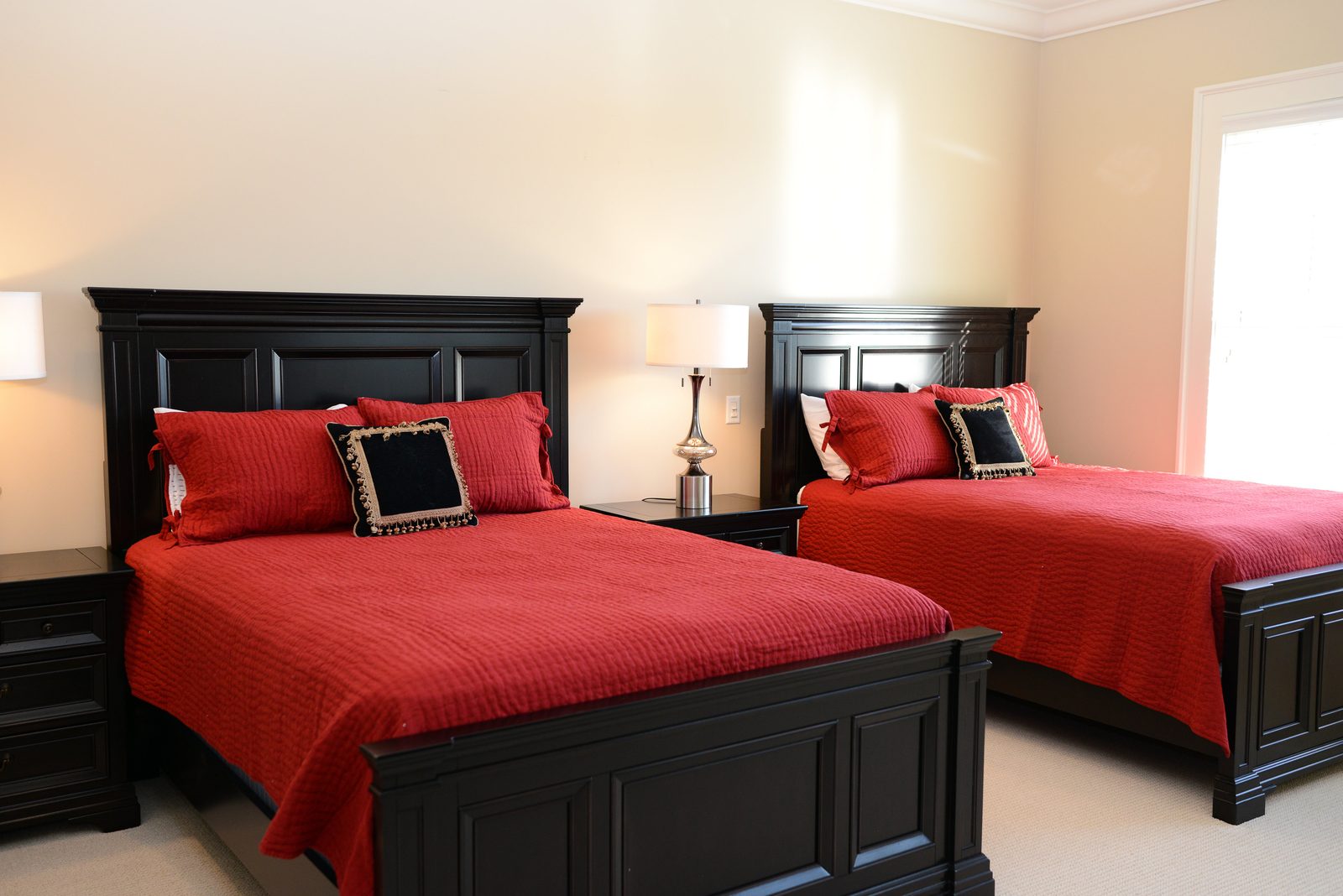 A guest room with two dark wood beds dressed in red linens and matching lamps (view 1)