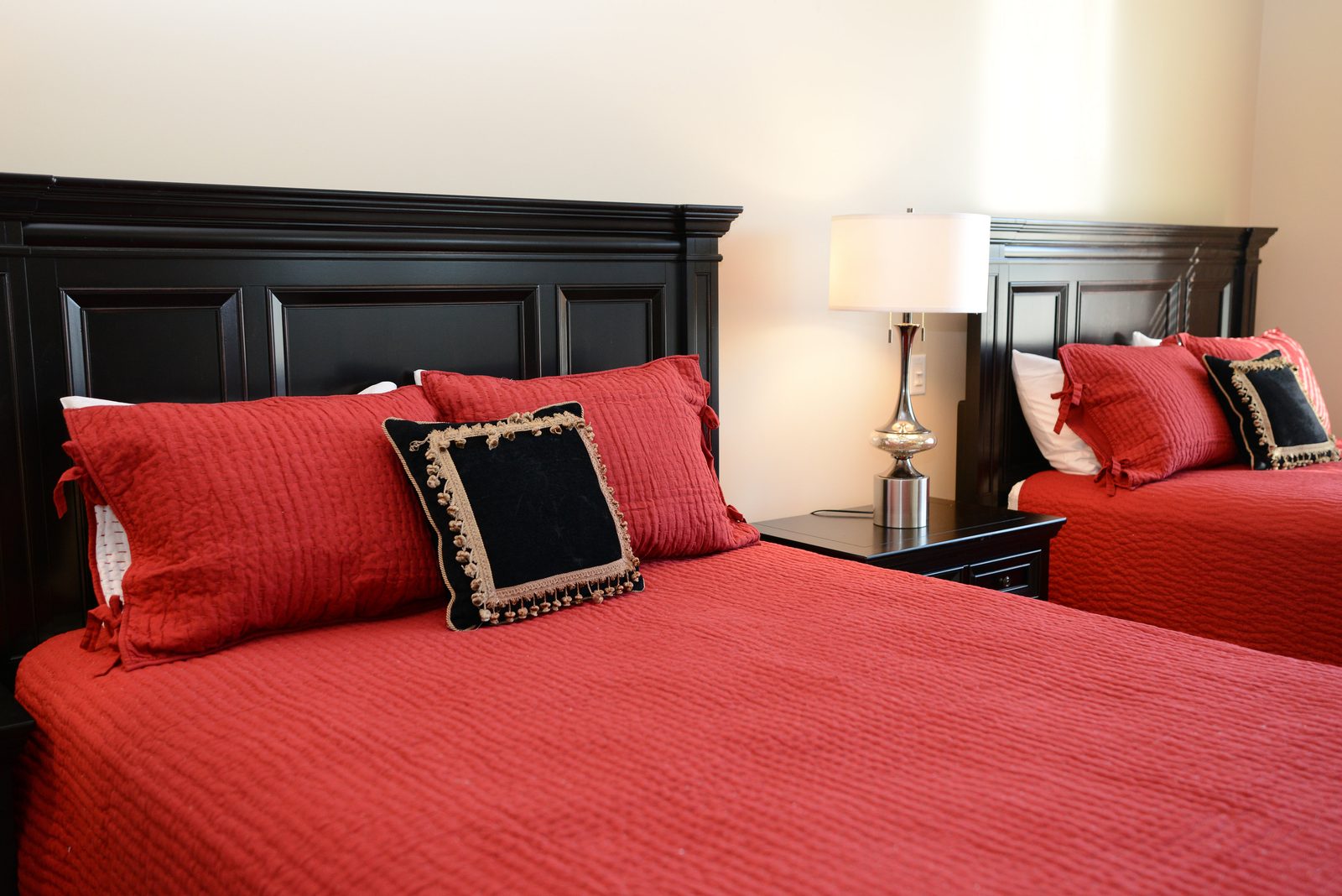 A guest room with two dark wood beds dressed in red linens and matching lamps (view 2)