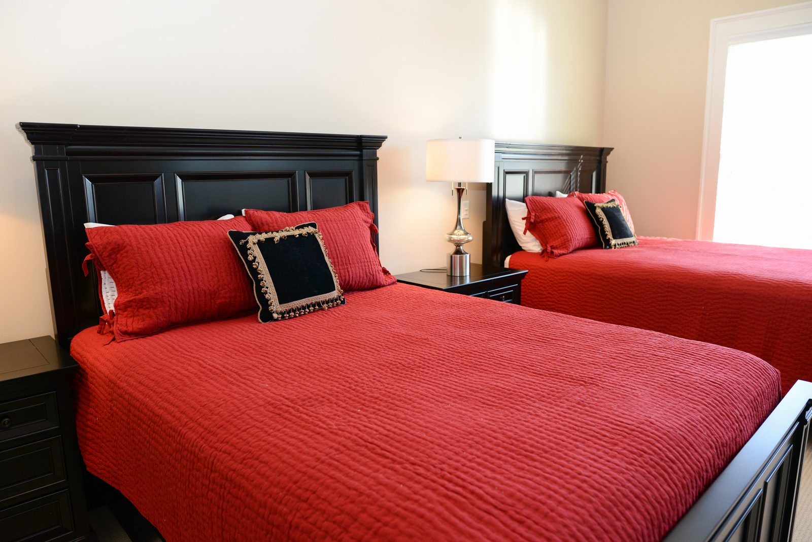 A guest room with two dark wood beds dressed in red linens and matching lamps (view 3)