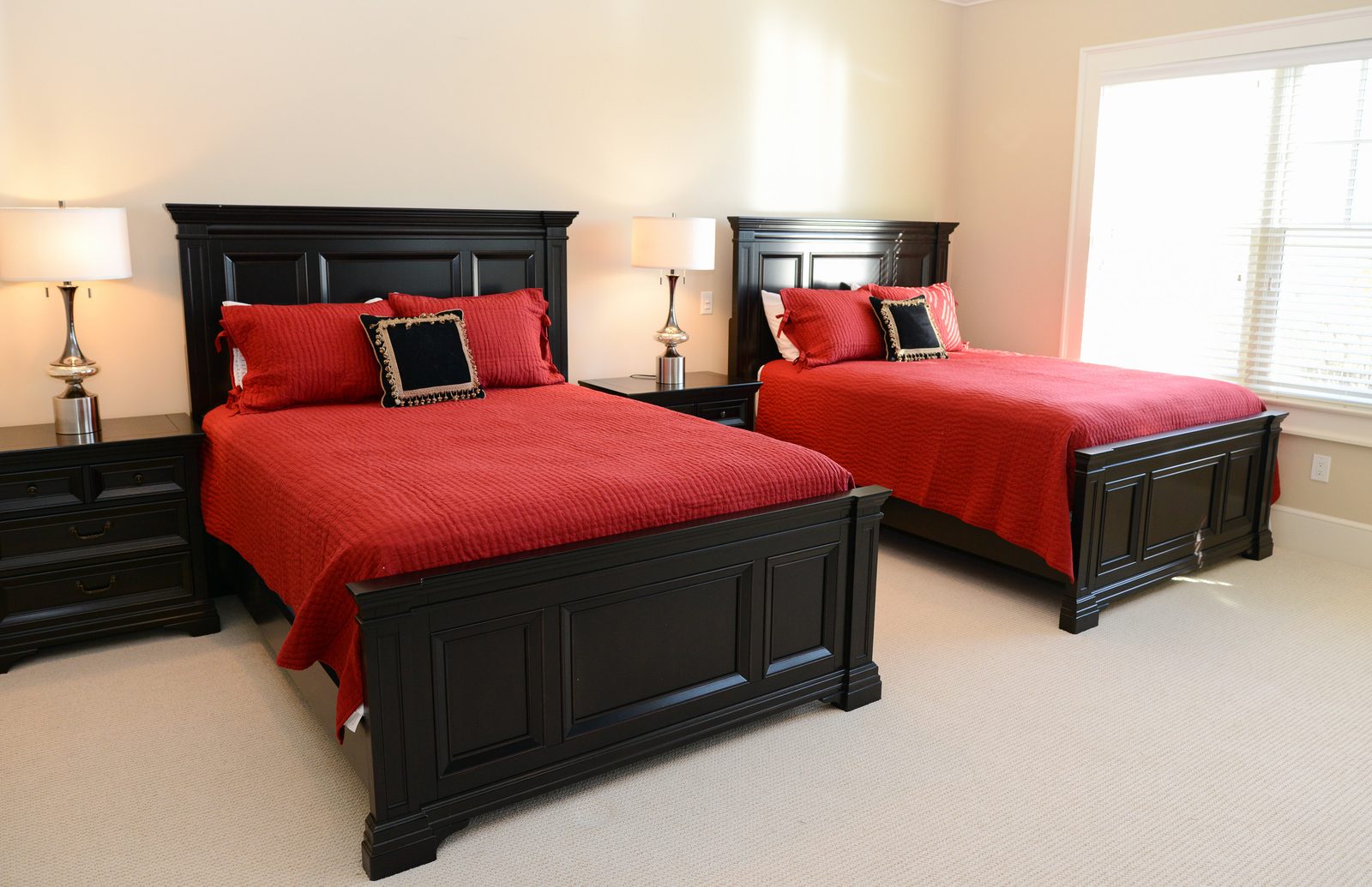A guest room with two dark wood beds dressed in red linens and matching lamps (view 4)