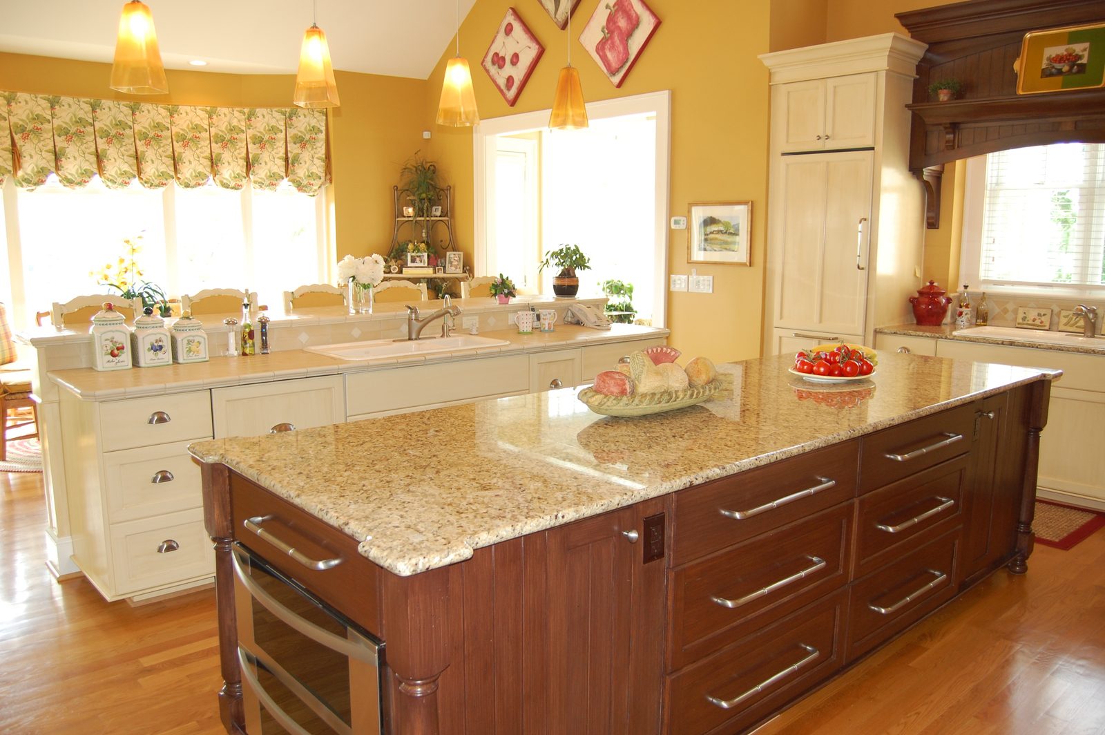A kitchen island with a granite counter and cream cabinetry beyond