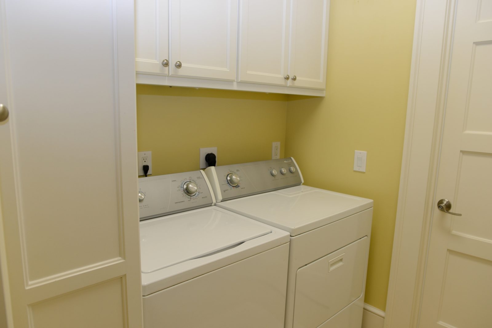 A laundry alcove with a washer, dryer and upper cabinets