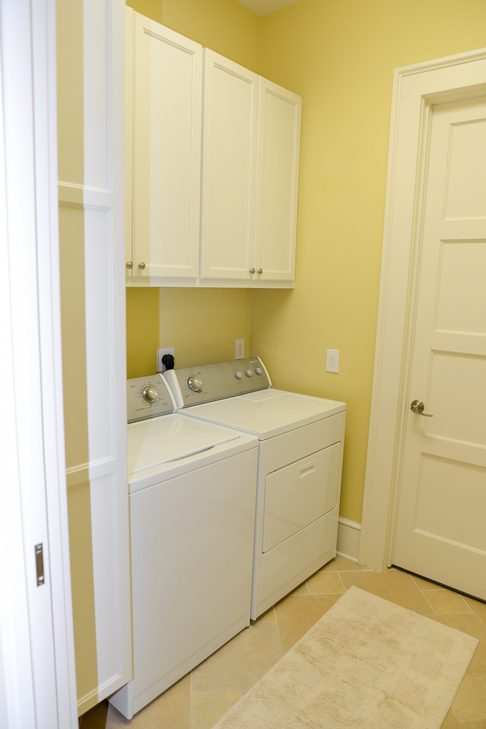 A laundry closet with a stacked washer and dryer and overhead cabinets