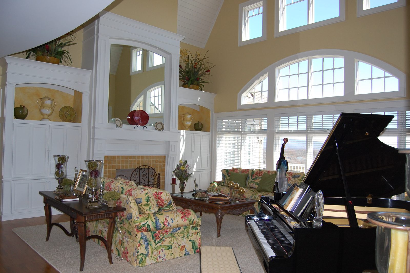A music room with a grand piano, floral seating and arched windows