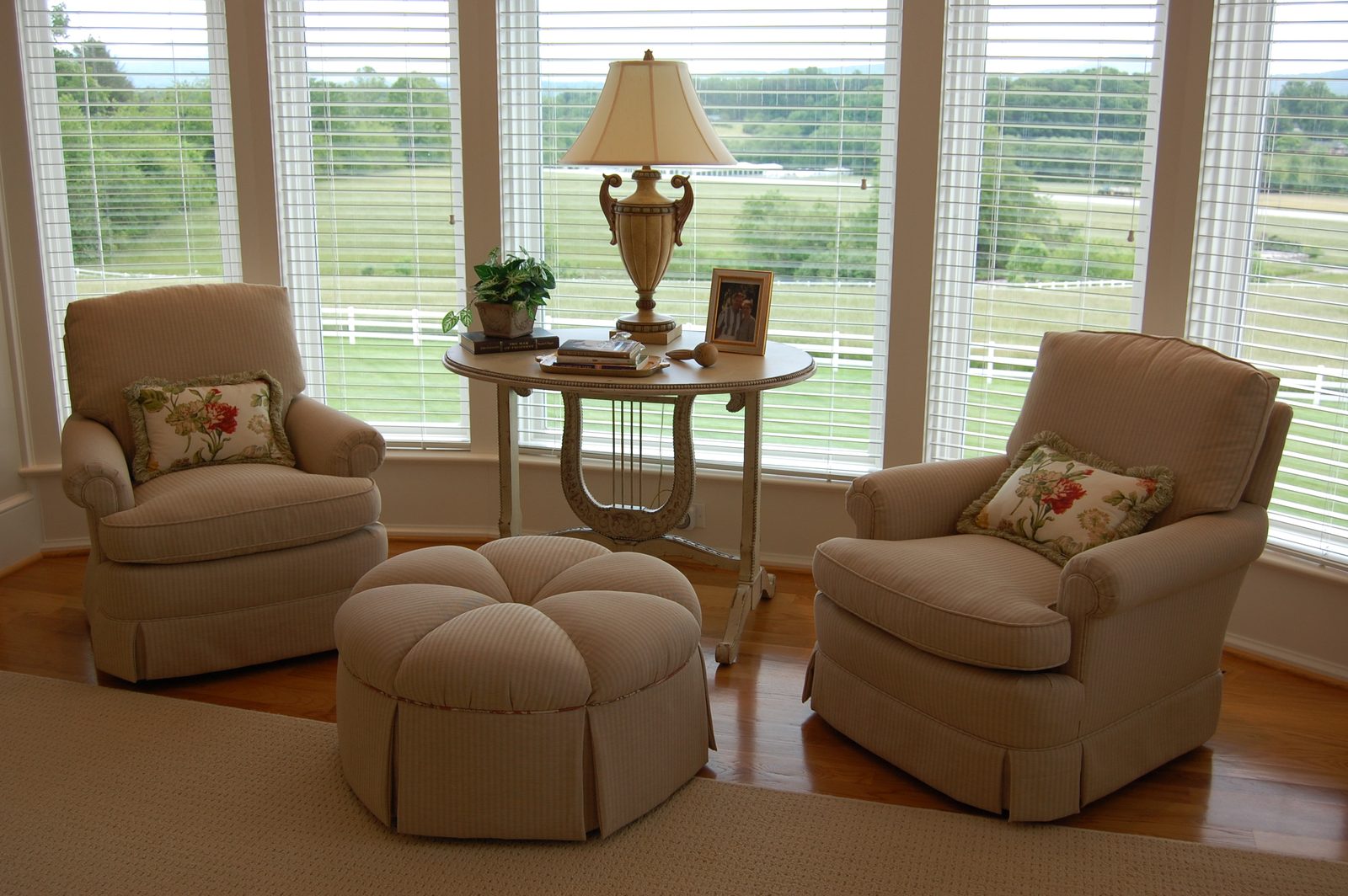 A sitting area with two armchairs and a round ottoman facing windows over the pasture