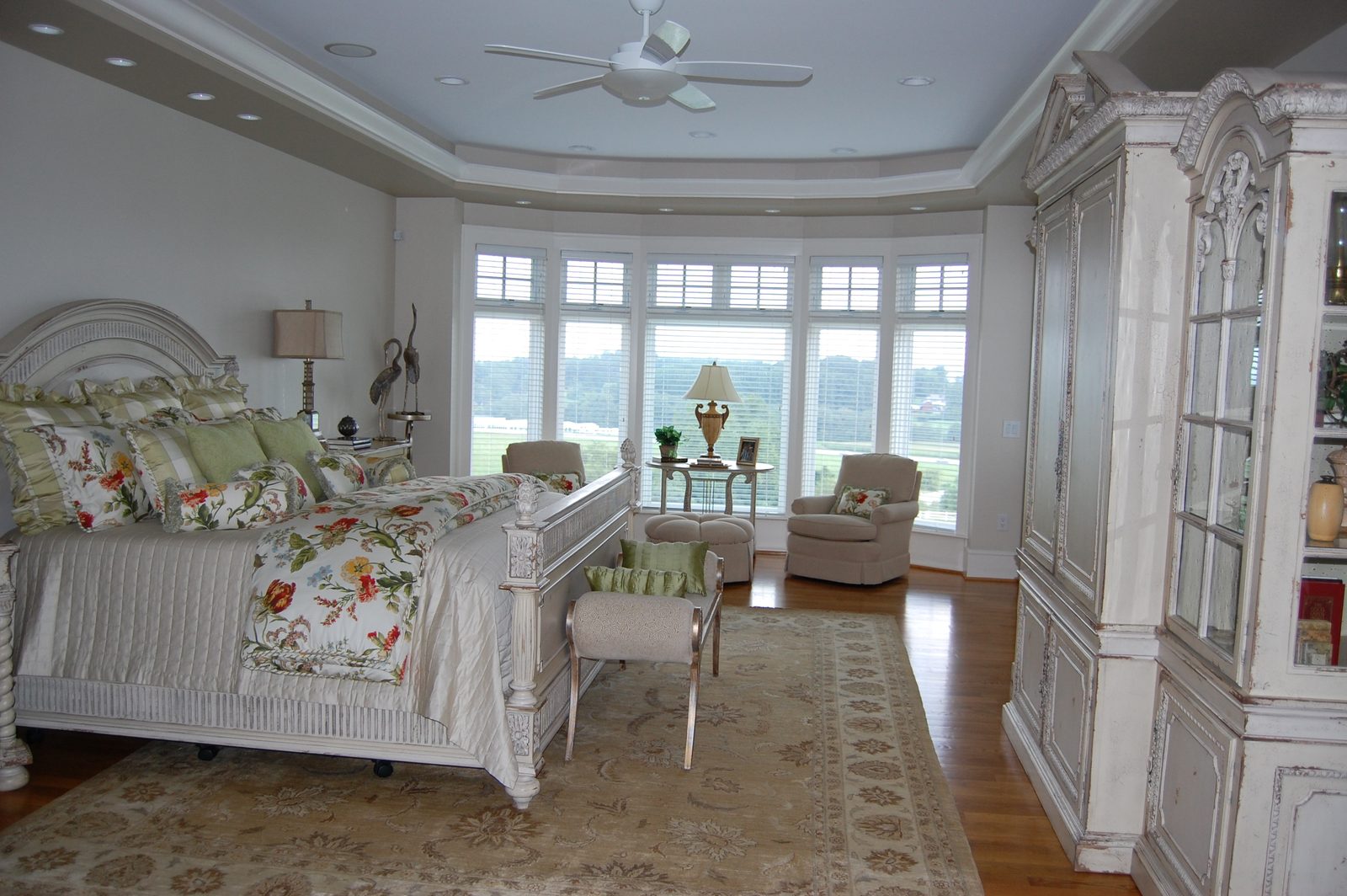 A large suite with a white bed, floral linens and a curved bay of windows