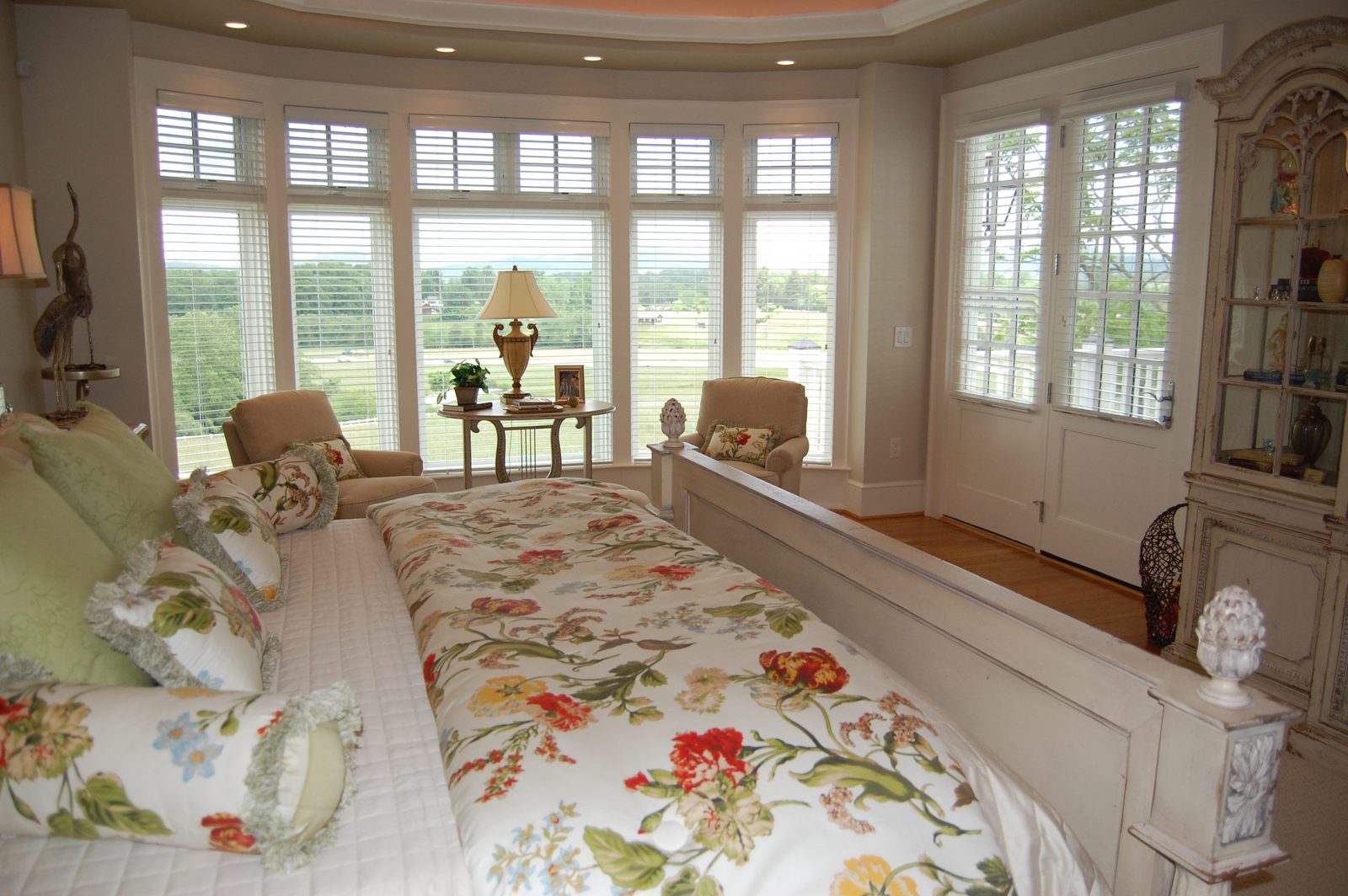 A suite with floral-linened beds facing a bay of windows over the fields