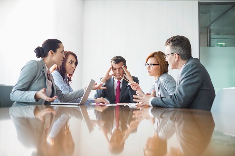 Stressed businessman sitting in the middle of coworkers during a meeting