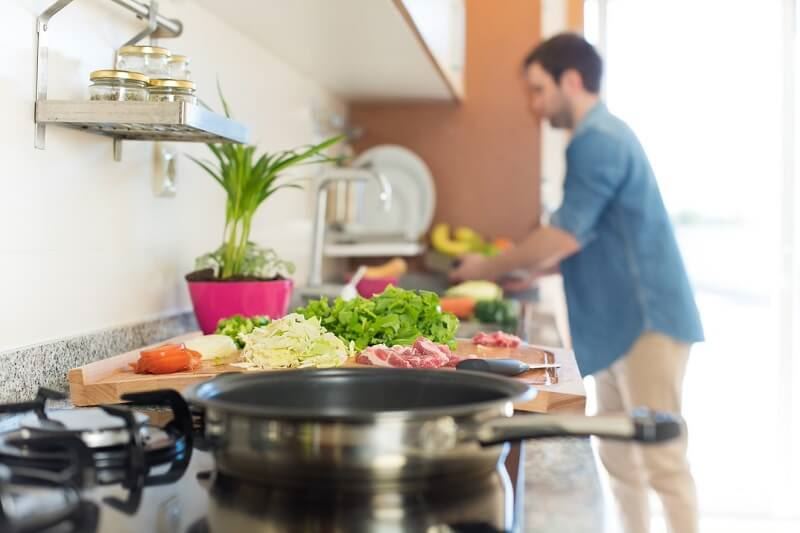 Focused picture of food on cutting board with gentlemen in the background continuing to prep