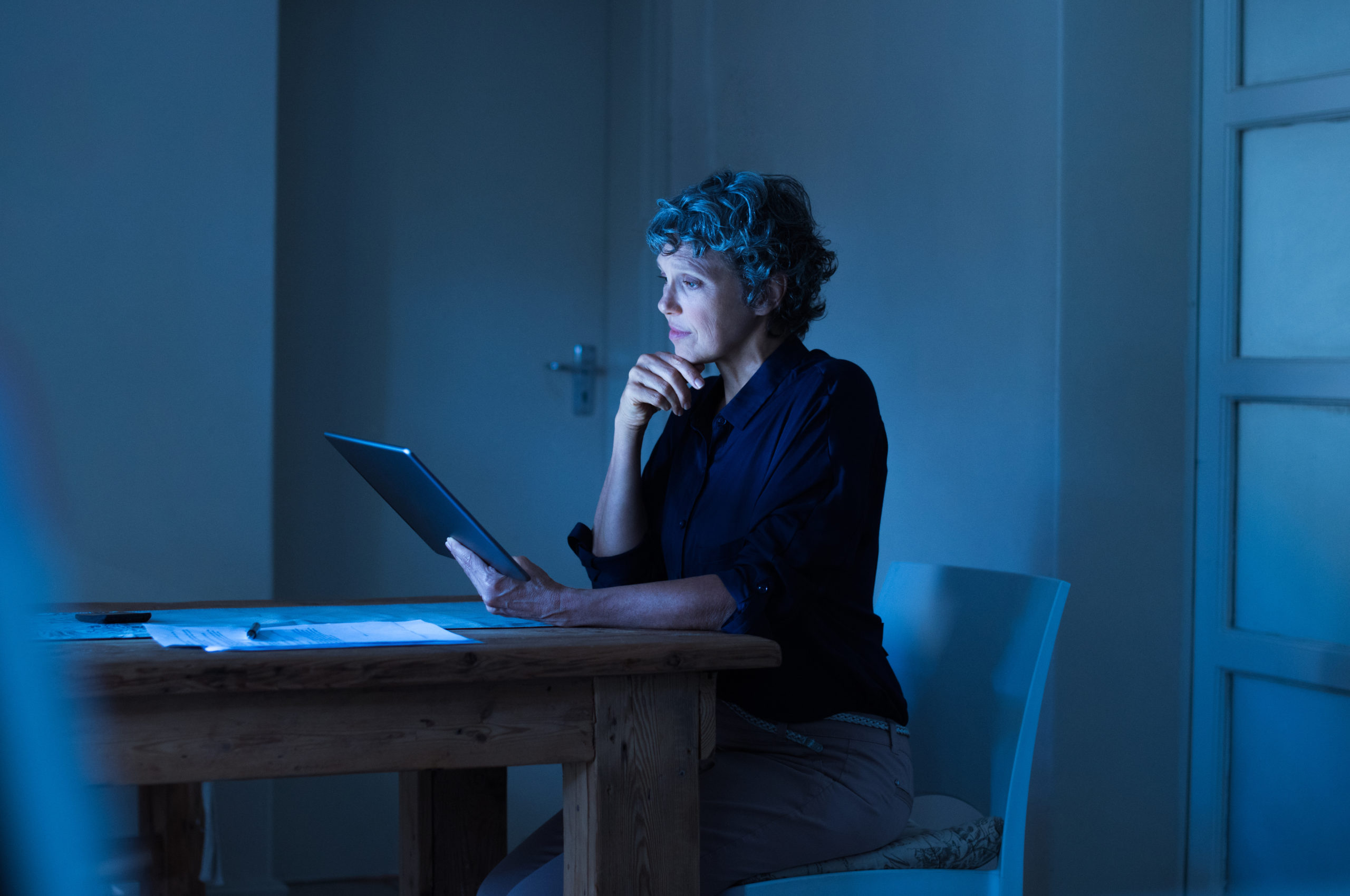 Thoughtful senior businesswoman working on digital tablet until late. Mature woman examining business report on laptop screen. Senior woman in formals using digital tablet at home during the night.