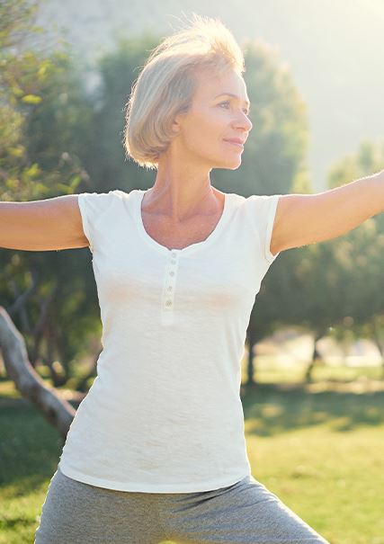 Older caucasian woman practicing a yoga pose outside in the sunlight