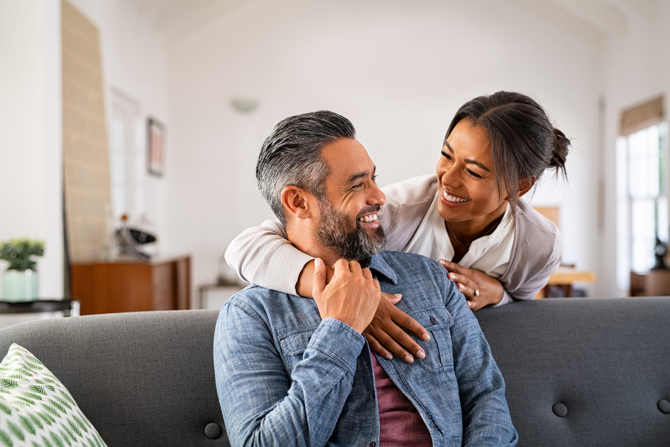 smiling-ethnic-woman-hugging-her-husband-on-the-couch-from-behind-in-the-living-room-middle-eastern-man-having-fun-with-his-beautiful-young-wife-on-the-couch-mid-adult-indian-man-with-latin-woman-laug-stockpack-istock