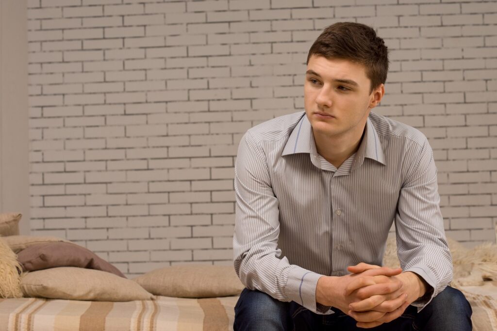 Stylish handsome young man sitting on a sofa thinking staring off to the side in contemplation against a brick wall with copyspace
