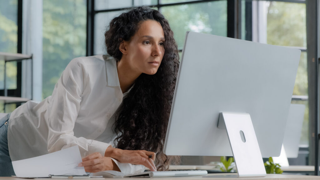 Young attractive hispanic woman professional manager developer working in modern office focused businesswoman checking electronic information on computer using paper documents researching sales data. High quality 4k footage