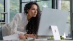 Young attractive hispanic woman professional manager developer working in modern office focused businesswoman checking electronic information on computer using paper documents researching sales data. High quality 4k footage