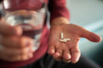Close up of man holding Soma pills in one hand with a glass of water in the other hand