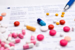 Various pills spread out on top of a paper on a table with a pen in the background