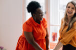 Two women laughing and smiling as one acts as a sober coach for the other