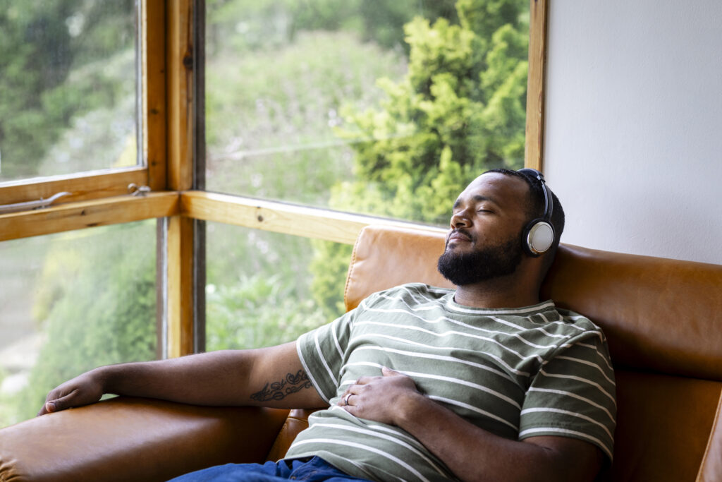 Man lounging on couch listening to music with headphones practicing self care as part of his recovery journey