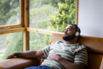 Man lounging on couch listening to music with headphones practicing self care as part of his recovery journey